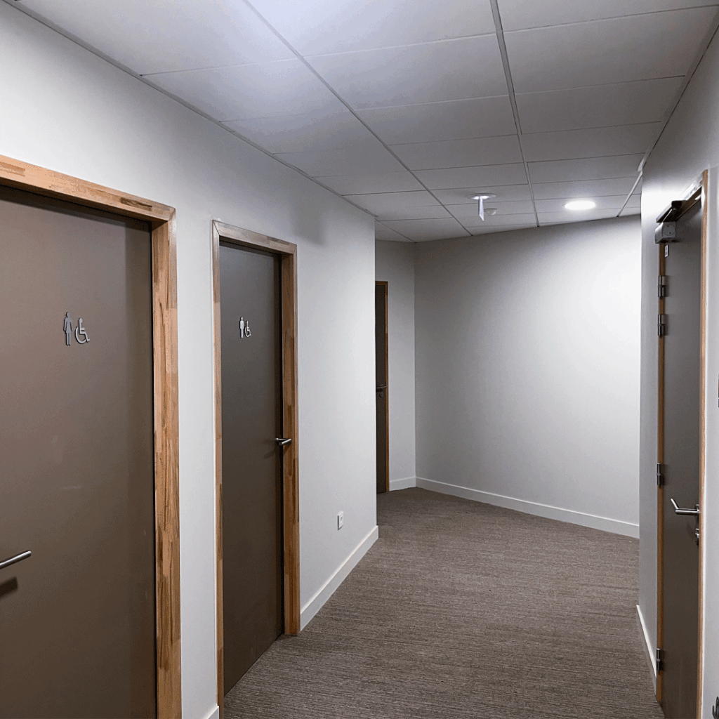 Signalétique de portes de toilettes avec pictogrammes homme, femme et accessibilité PMR dans un couloir de bureaux.
