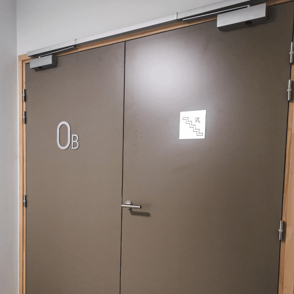 Signalétique sur porte double avec lettrage et pictogramme d'escalier pour l'orientation.