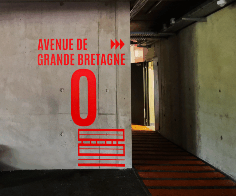 Adhésif rouge vif "AVENUE DE GRANDE BRETAGNE" un mur de béton, signalétique murale et d'orientation par Global Signa France.