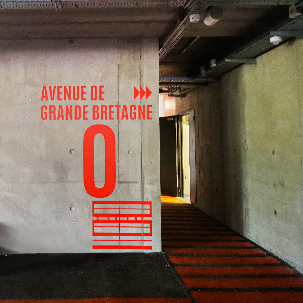 Signalétique directionnelle et niveau de parking en adhésif rouge sur un mur en béton brut à la Cartoucherie.