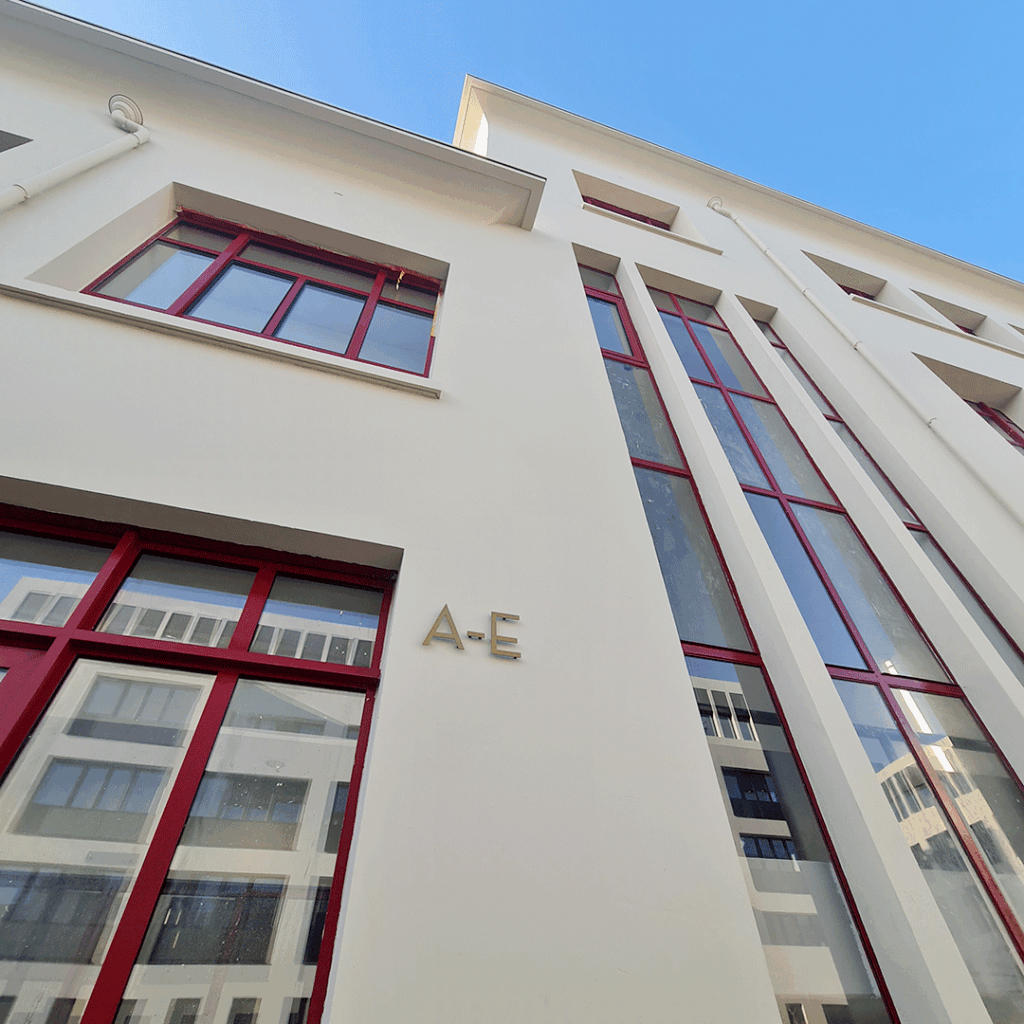 Signalétique extérieure: identification de zone A-E en lettres 3D métalliques sur façade moderne avec fenêtres rouges.