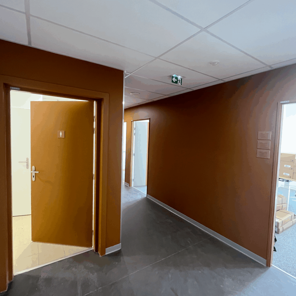 Signalétique de bureau simple en adhésif ou plaque sur porte en bois clair dans un couloir moderne d'entreprise.
