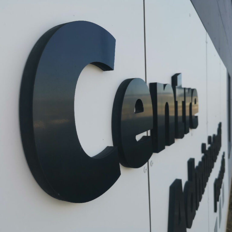 Lettres boîtiers découpées en relief (3D) noires, fixées sur une façade blanche pour une signalétique d'entreprise haut de gamme.