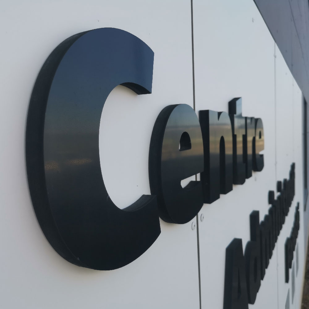 Lettres boîtiers découpées en relief (3D) noires, fixées sur une façade blanche pour une signalétique d'entreprise haut de gamme.