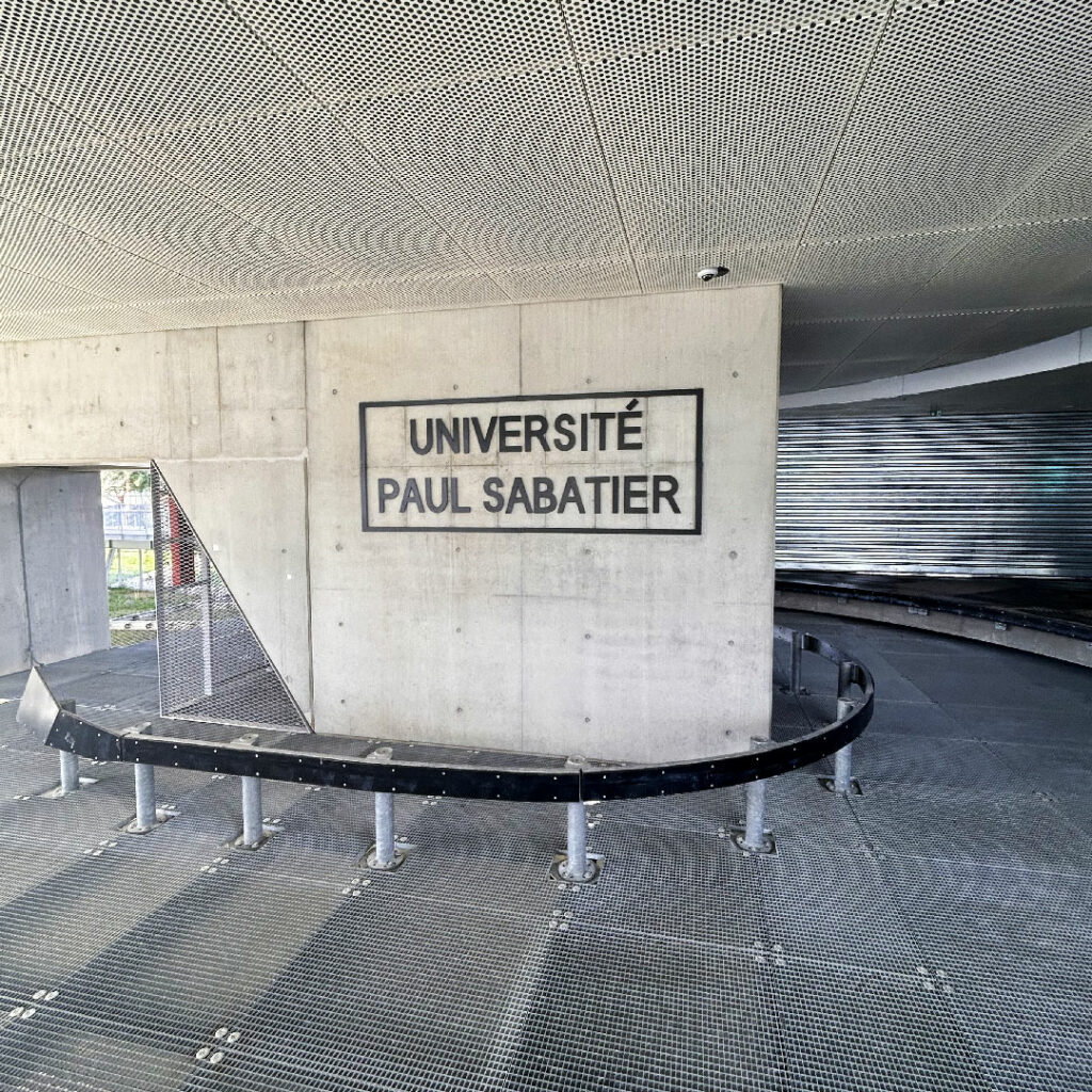Enseigne de signalétique de l'Université Paul Sabatier sur un mur en béton brut, dans un hall d'entrée à l'architecture contemporaine à Toulouse.
