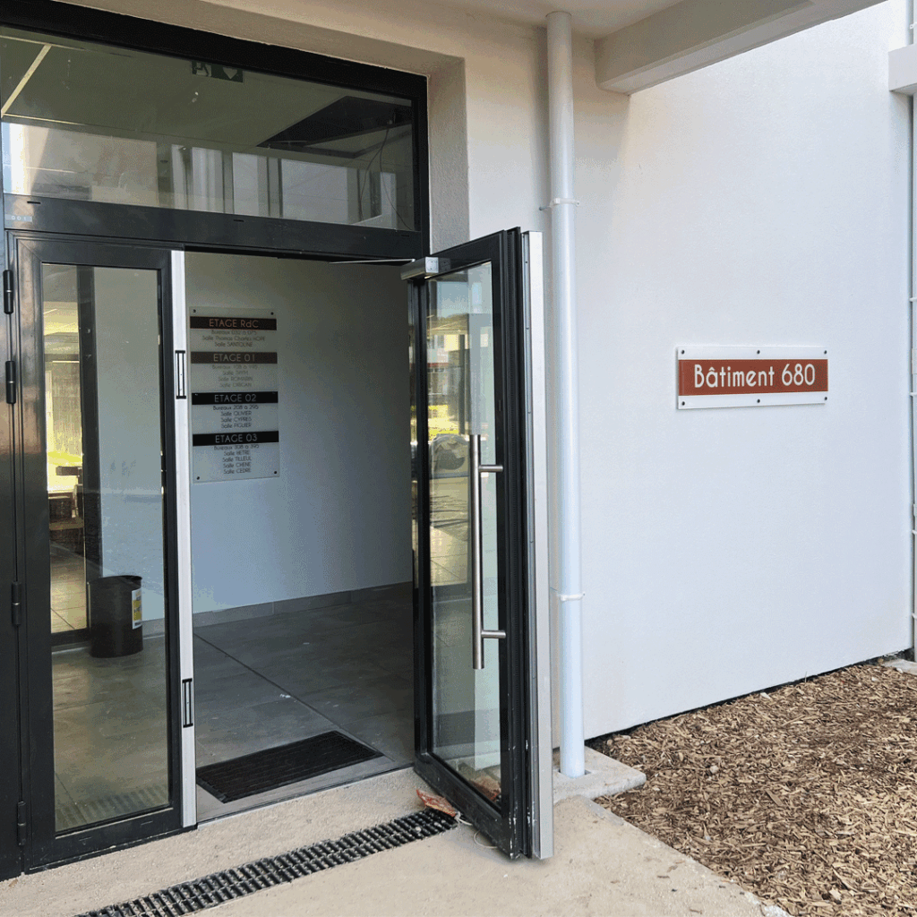 Enseigne murale extérieure de couleur rouille près d'une porte vitrée, indiquant l'entrée d'un local professionnel.