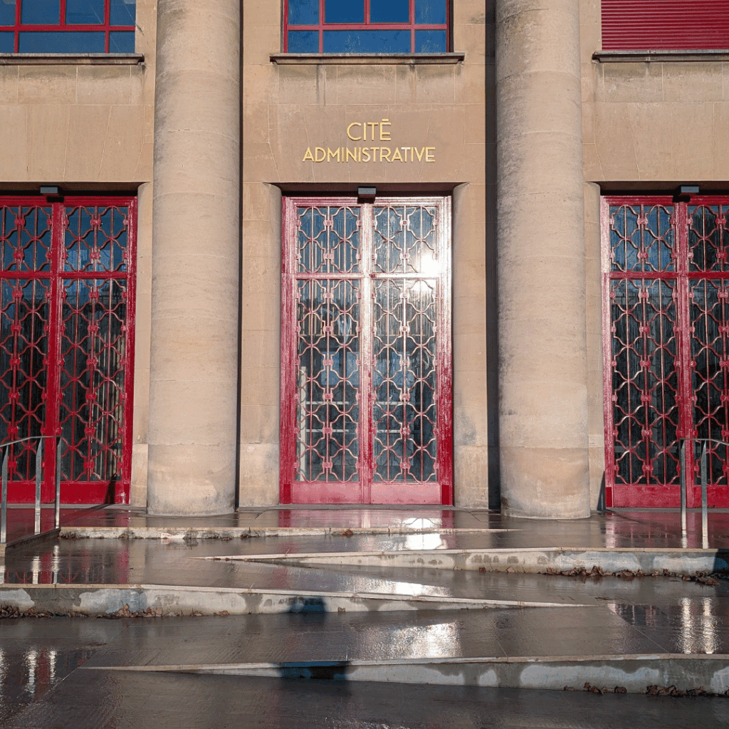 Façade classique de la Cité Administrative de Toulouse, avec colonnes, portes rouges et signalétique relief en couleur or.