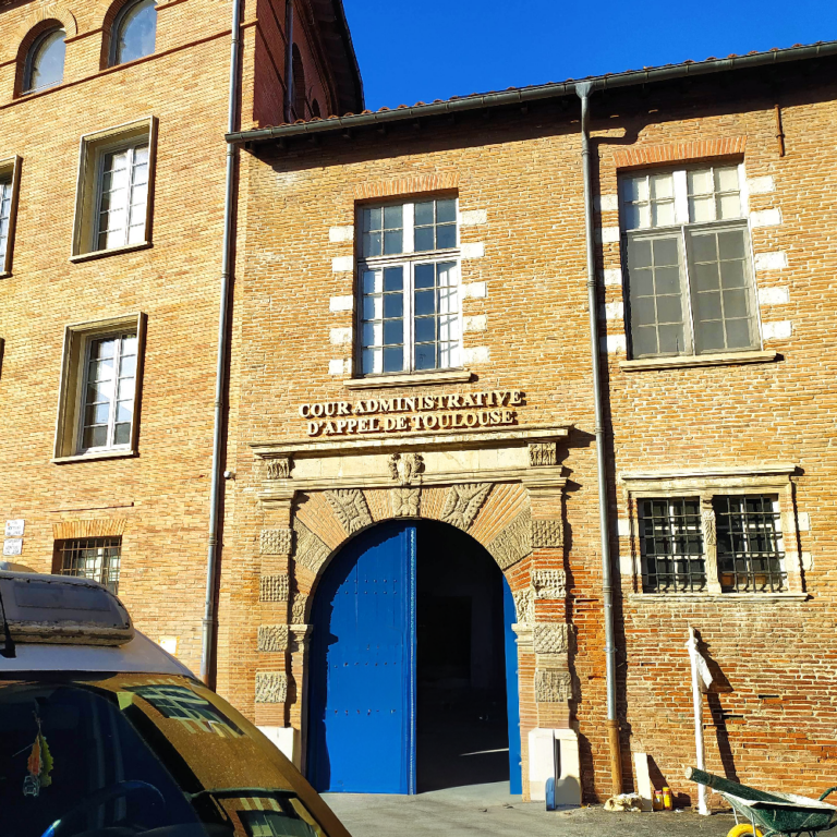 Façade en briques d'un bâtiment institutionnel (Cour Administrative d'Appel de Toulouse) avec enseigne de pierre au-dessus de la porte bleue.