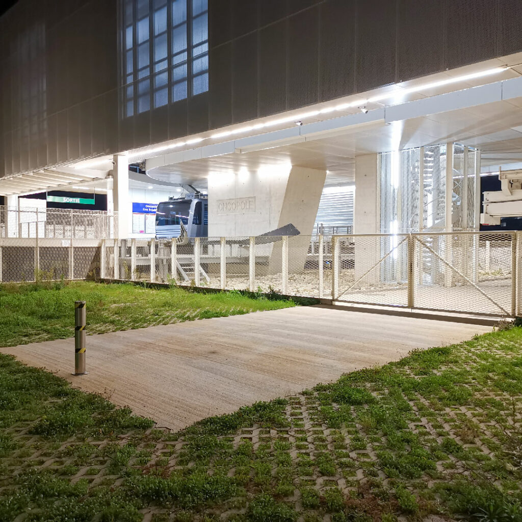 Station du téléphérique de Toulouse la nuit, avec la signalétique de sortie et une cabine de transport visible derrière la grille.