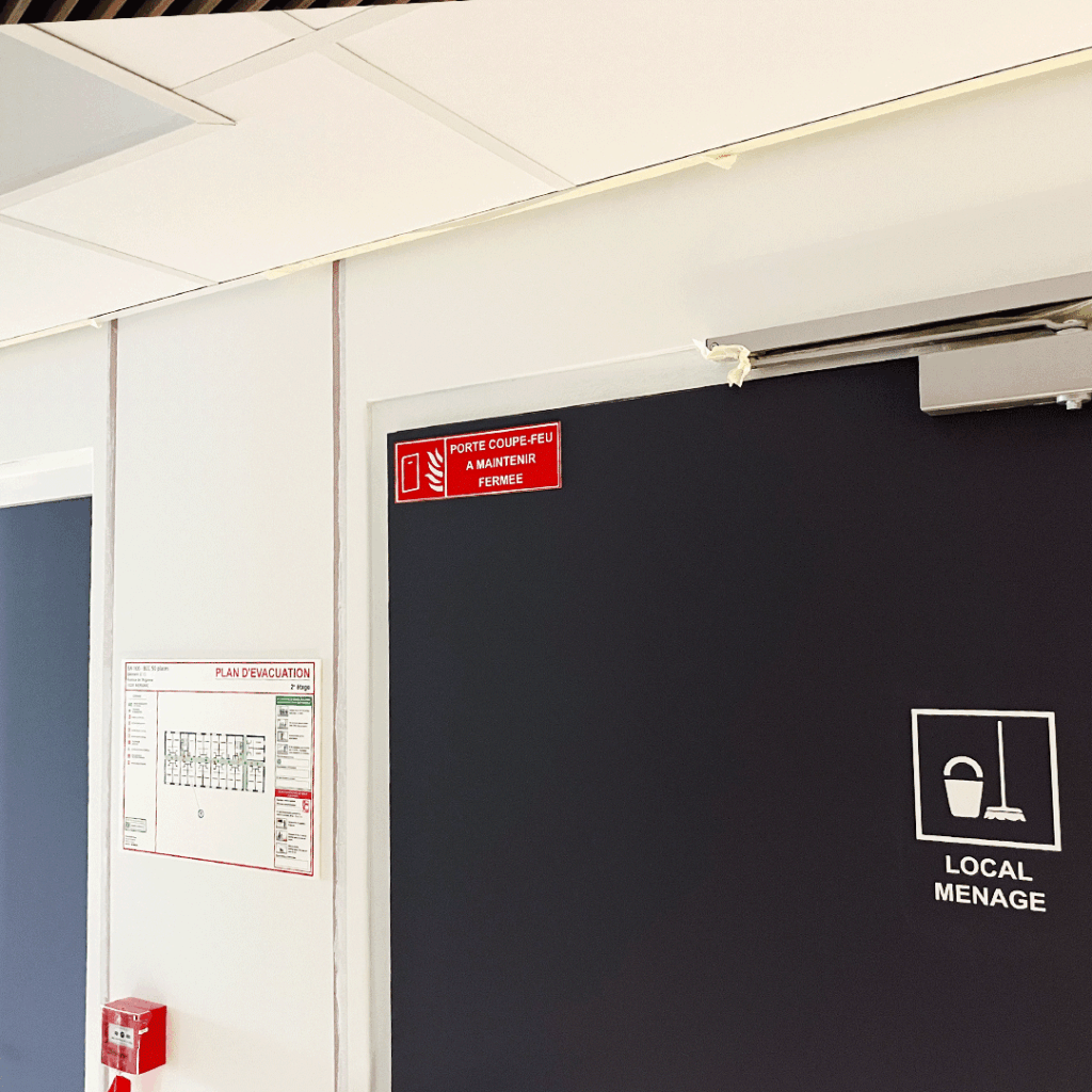 Signalétique de sécurité sur porte noire: panneau coupe-feu, plan d'évacuation, et pictogramme Local Ménage.