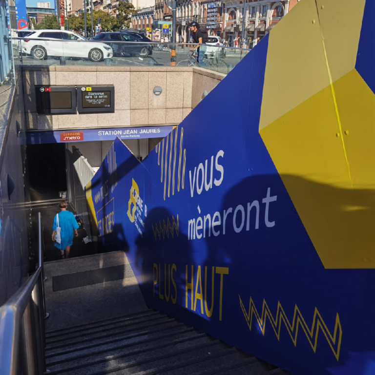 Grande palissade adhésive bleue et jaune devant l'entrée de la station de métro Jean Jaurès à Toulouse.