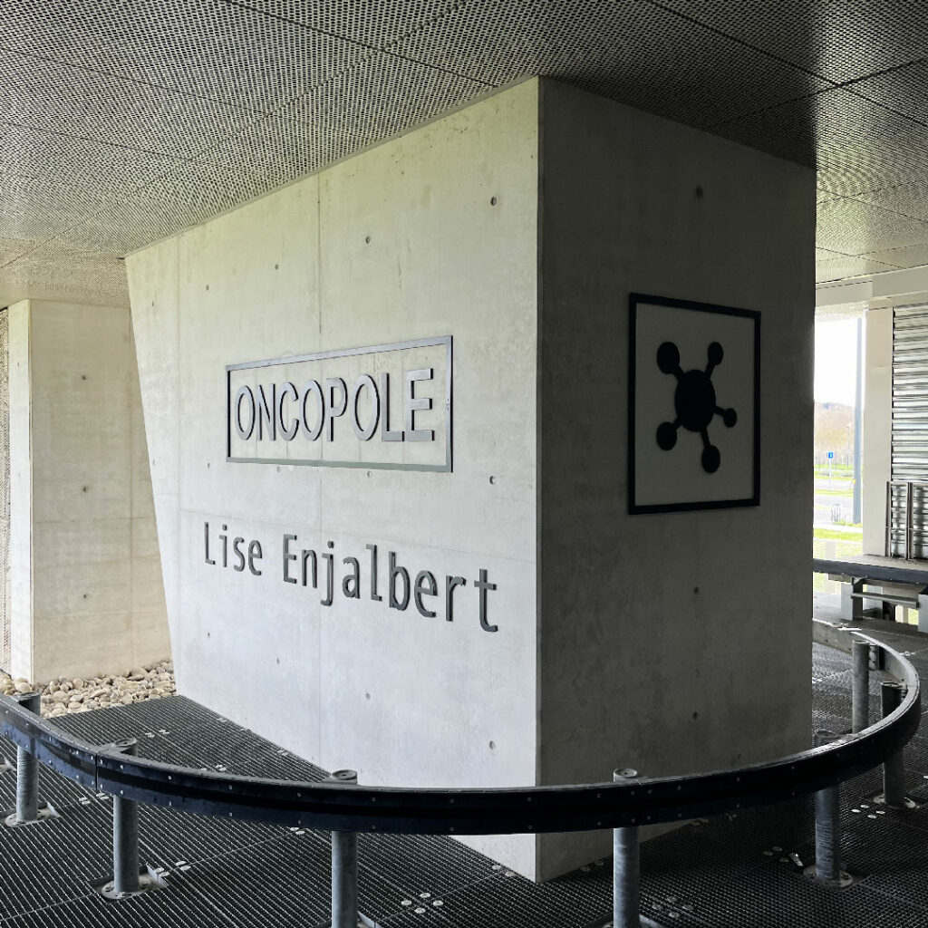 Enseigne de signalétique interne Oncopole Lise Enjalbert sur pilier en béton avec logo, dans un hall à l'architecture moderne et épurée.
