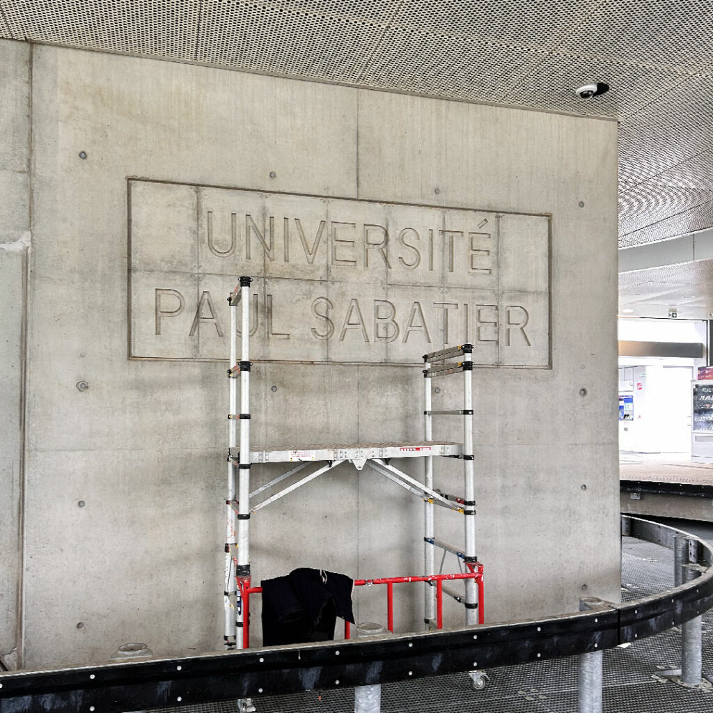 Échafaudage devant l'empreinte de la signalétique murale Université Paul Sabatier, montrant les étapes de la pose de l'enseigne.
