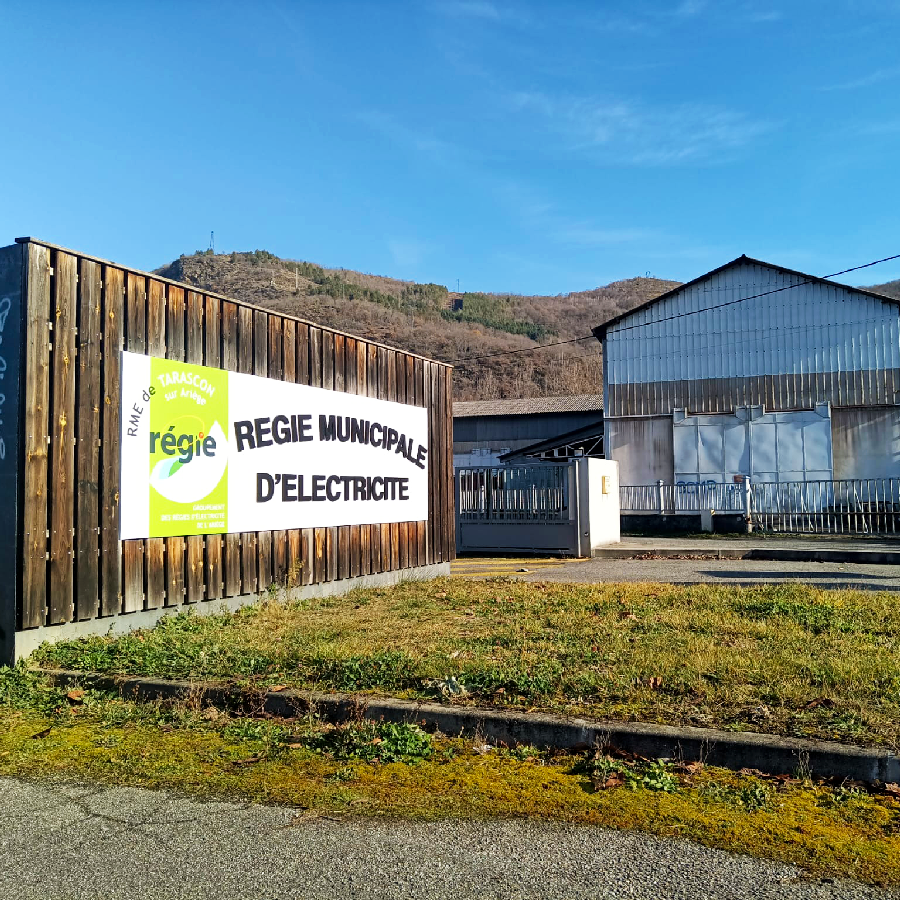 Panneau de grande signalétique RME de Tarascon sur Ariège affichant « REGIE MUNICIPALE D'ELECTRICITE » sur façade en bois.
