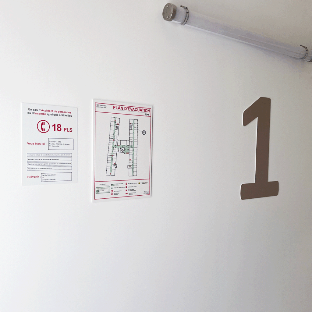 Plan d'évacuation et instructions de sécurité affichés sur un mur blanc à côté d'une grande numérotation d'étage.