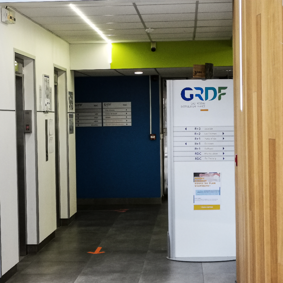 Totem de signalétique intérieure GRDF listant les services par étage (R+3, R+2, R+1) et affichant le plan d'évacuation.